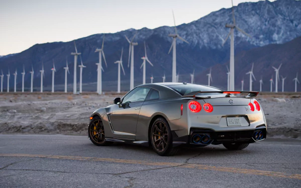 HD wallpaper of a Nissan GT-R parked on a road with a backdrop of wind turbines and mountains.