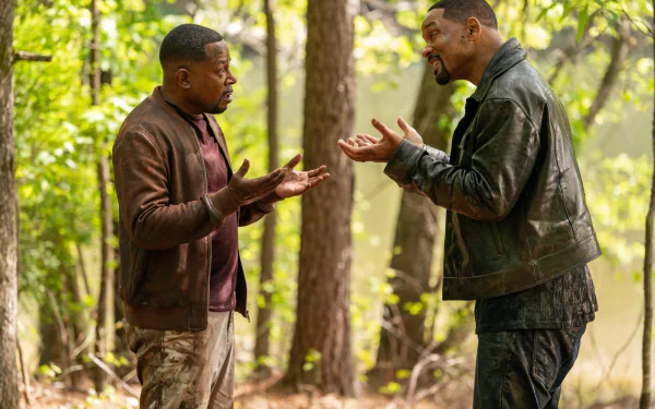 HD desktop wallpaper from the movie Bad Boys: Ride or Die featuring Will Smith and Martin Lawrence in a forest setting, engaging in an animated conversation.