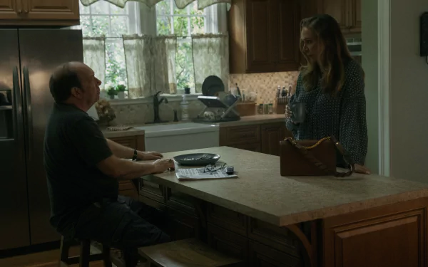 HD desktop wallpaper from the TV show Presumed Innocent (2024). A man and woman have a conversation in a cozy, well-lit kitchen with wooden cabinets and a central island.