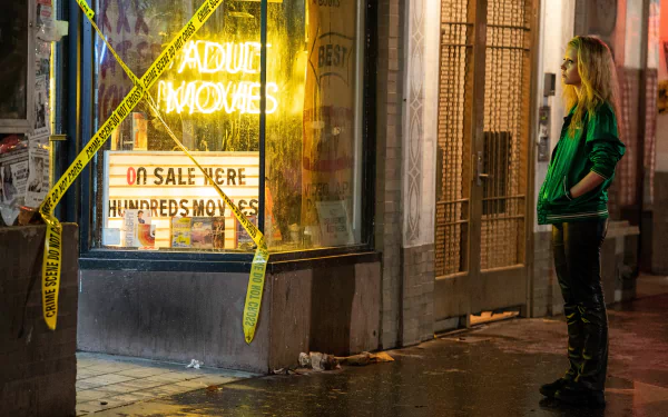 HD desktop wallpaper featuring Mia Goth as Maxxxine, standing in front of a neon-lit adult movie store at night, surrounded by yellow caution tape.