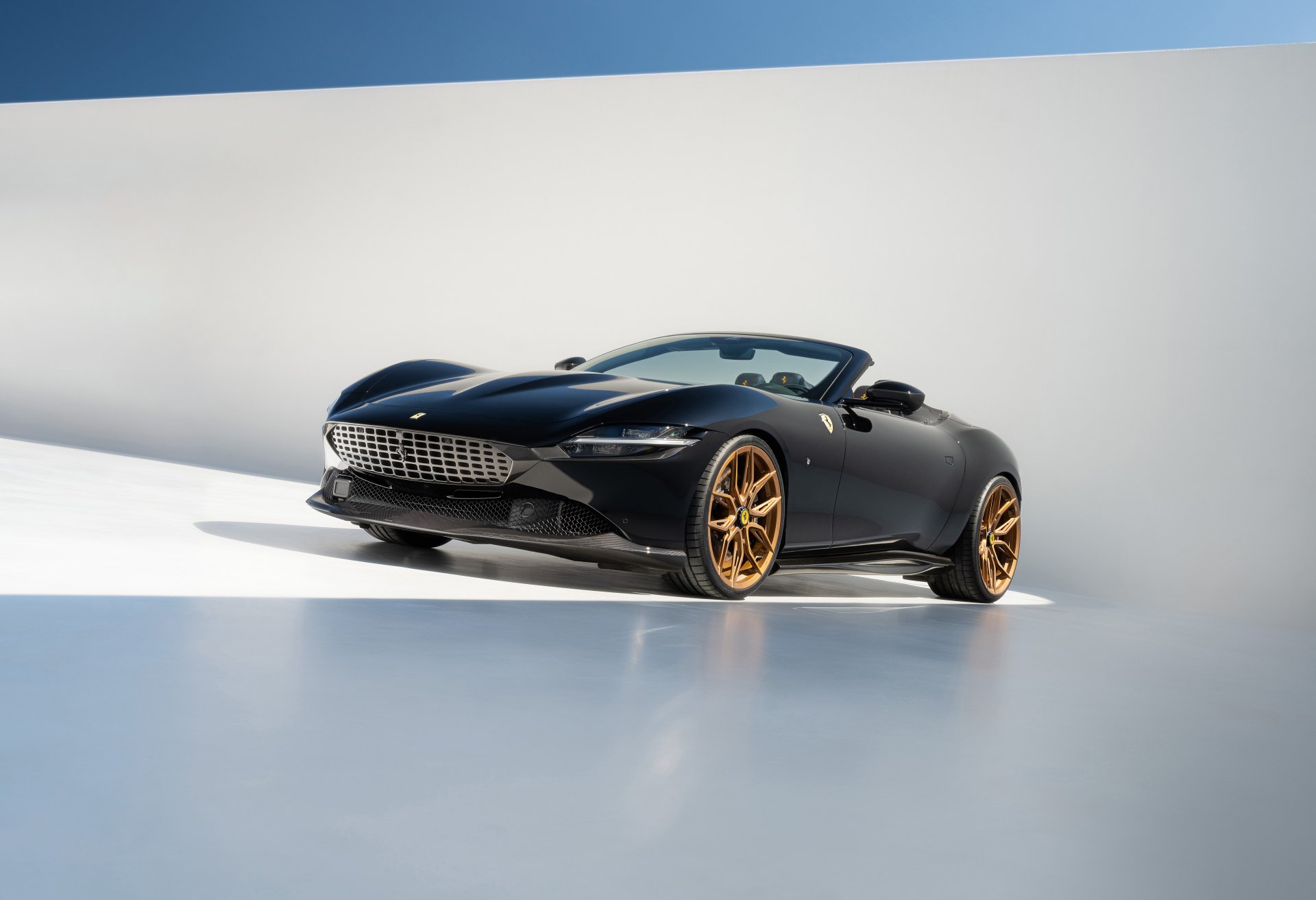 A sleek black Ferrari Roma with striking gold wheels is showcased in a modern, minimalist setting, serving as an eye-catching HD desktop wallpaper and background.