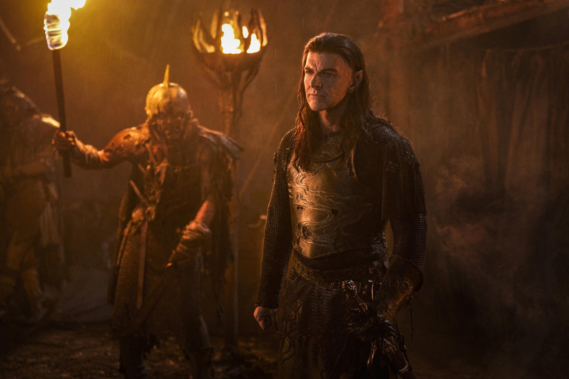 A dramatic scene from *The Lord of the Rings: The Rings of Power*, featuring armored characters in a dimly lit environment, evoking the series' epic fantasy atmosphere.