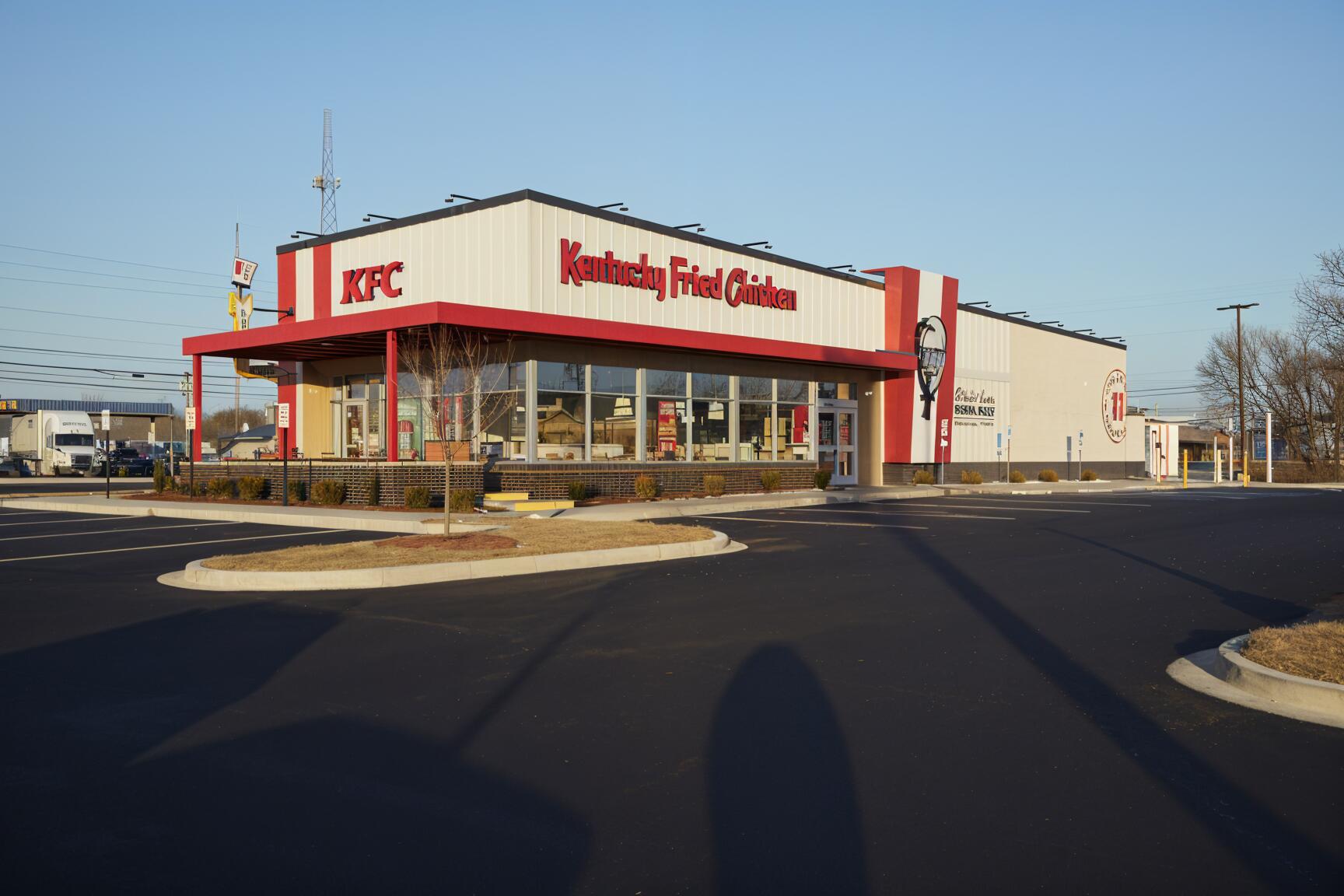 A vibrant HD desktop wallpaper featuring a KFC restaurant, showcasing the iconic red and white building against a clear sky and freshly paved parking lot.