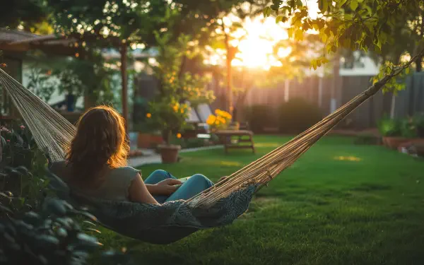 A serene backyard scene featuring a person relaxing in a hammock as the sun sets, creating a warm and tranquil atmosphere, captured in vibrant 4K Ultra HD.