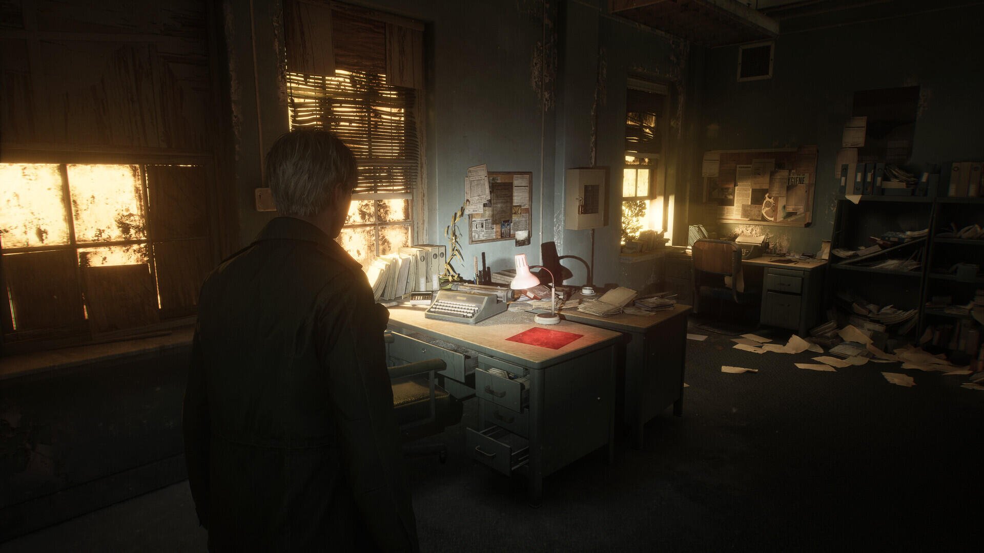 A moody, atmospheric scene from Silent Hill 2, featuring a character standing in a cluttered, dimly lit office filled with scattered papers and warm light filtering through the windows.