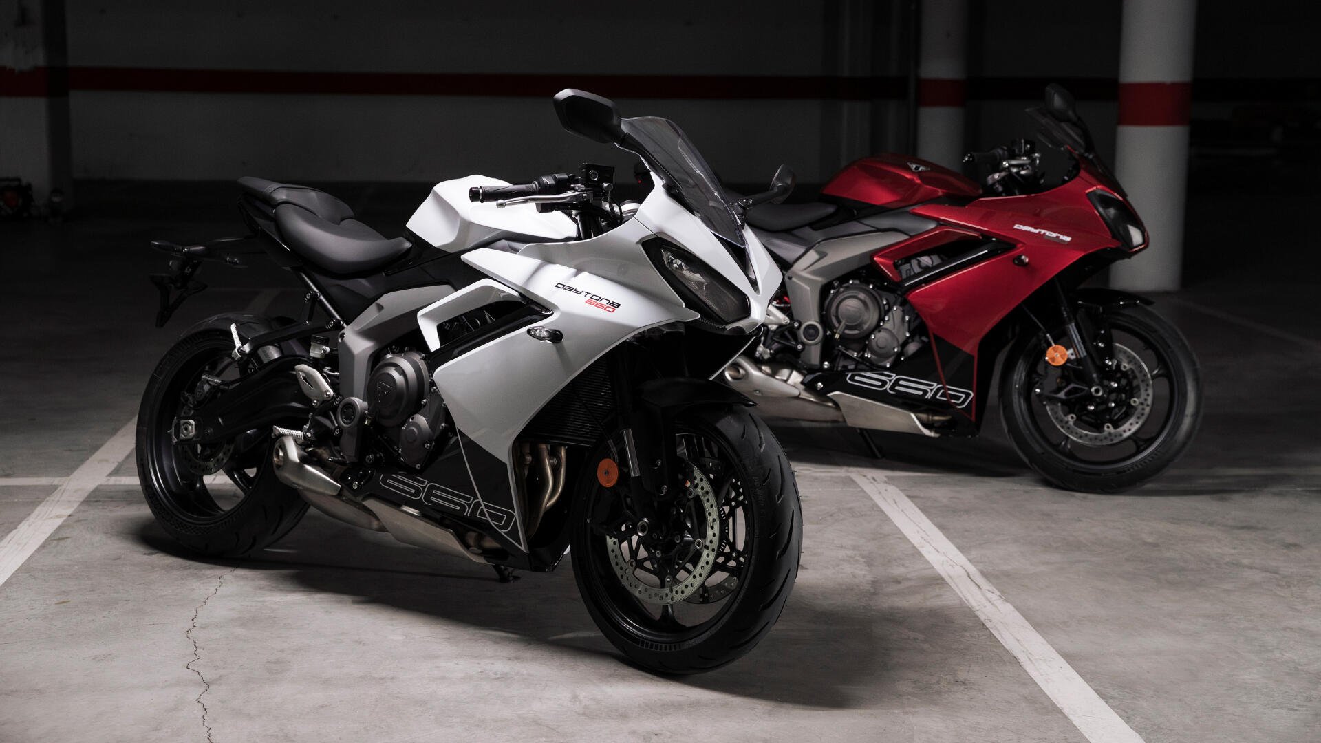 A striking image of two Triumph Daytona 660 motorcycles, one in white and the other in red, set against a minimalist parking garage backdrop. Captured in 4K Ultra HD.