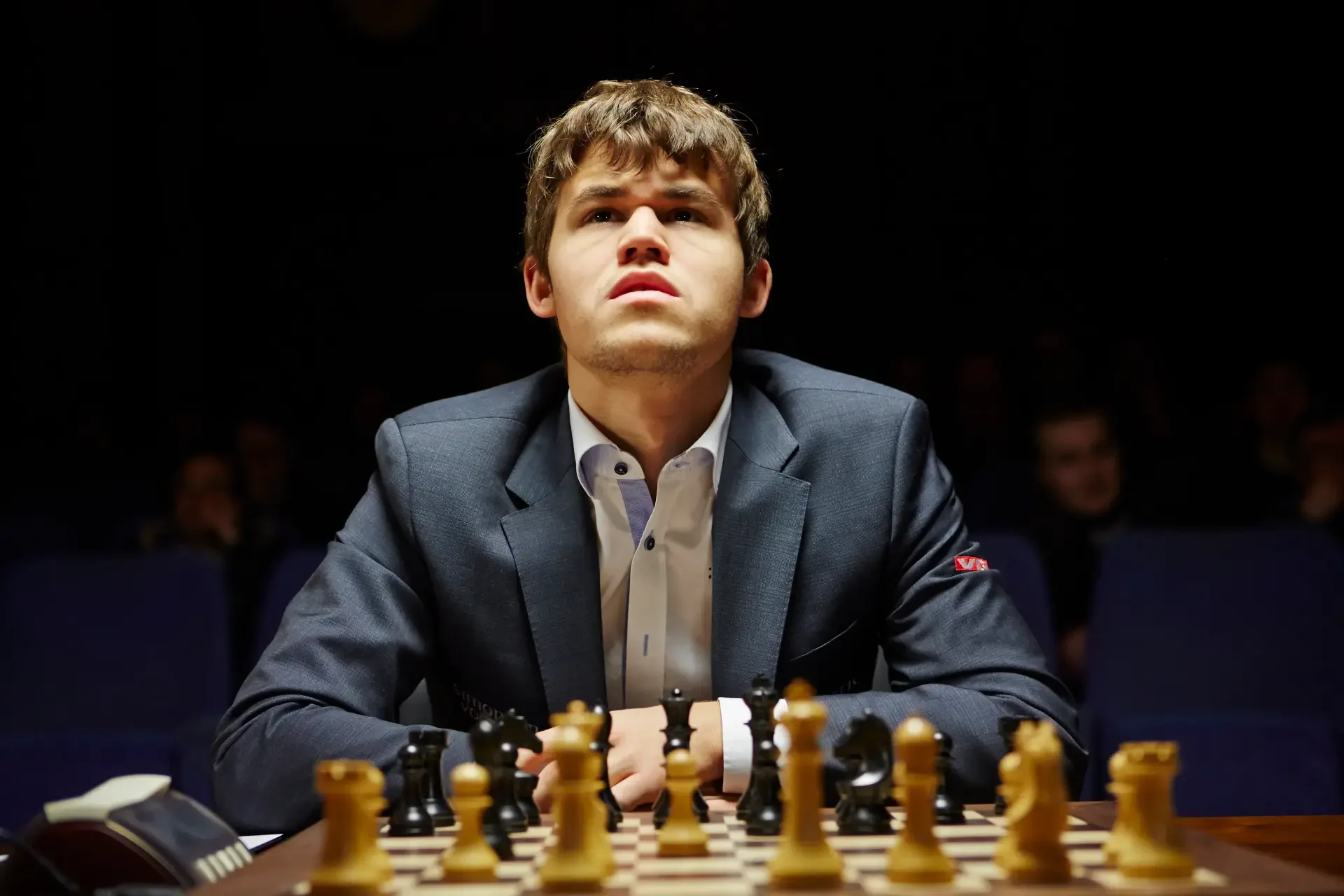 Magnus Carlsen concentrates intently at a chessboard, surrounded by pieces, capturing the intensity of competitive chess. This striking image serves as a captivating 4K Ultra HD wallpaper.