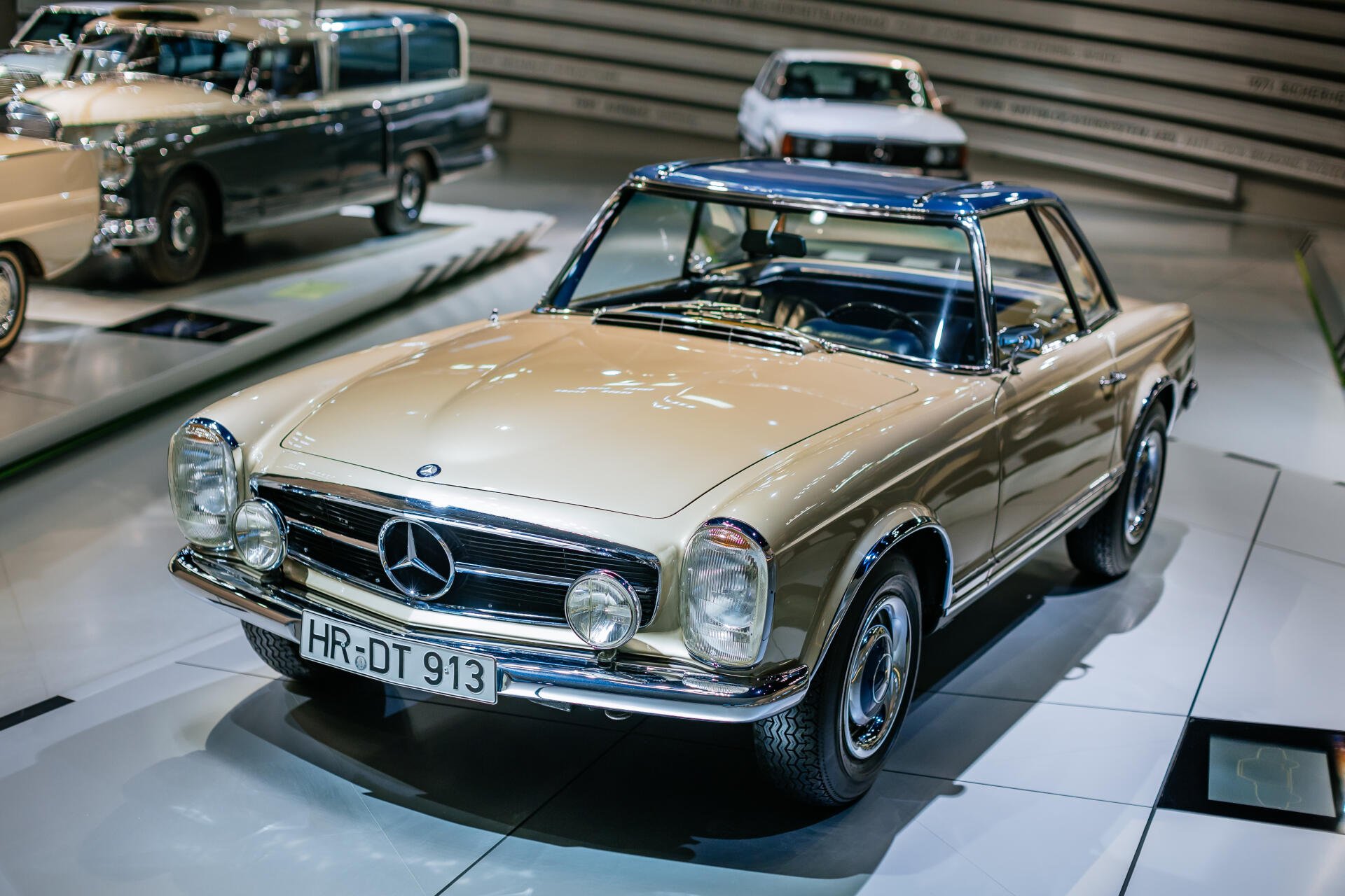 A classic Mercedes-Benz 230 SL showcased in a sleek, modern setting, featuring a striking gold exterior and a blue roof, captured in 4K Ultra HD.