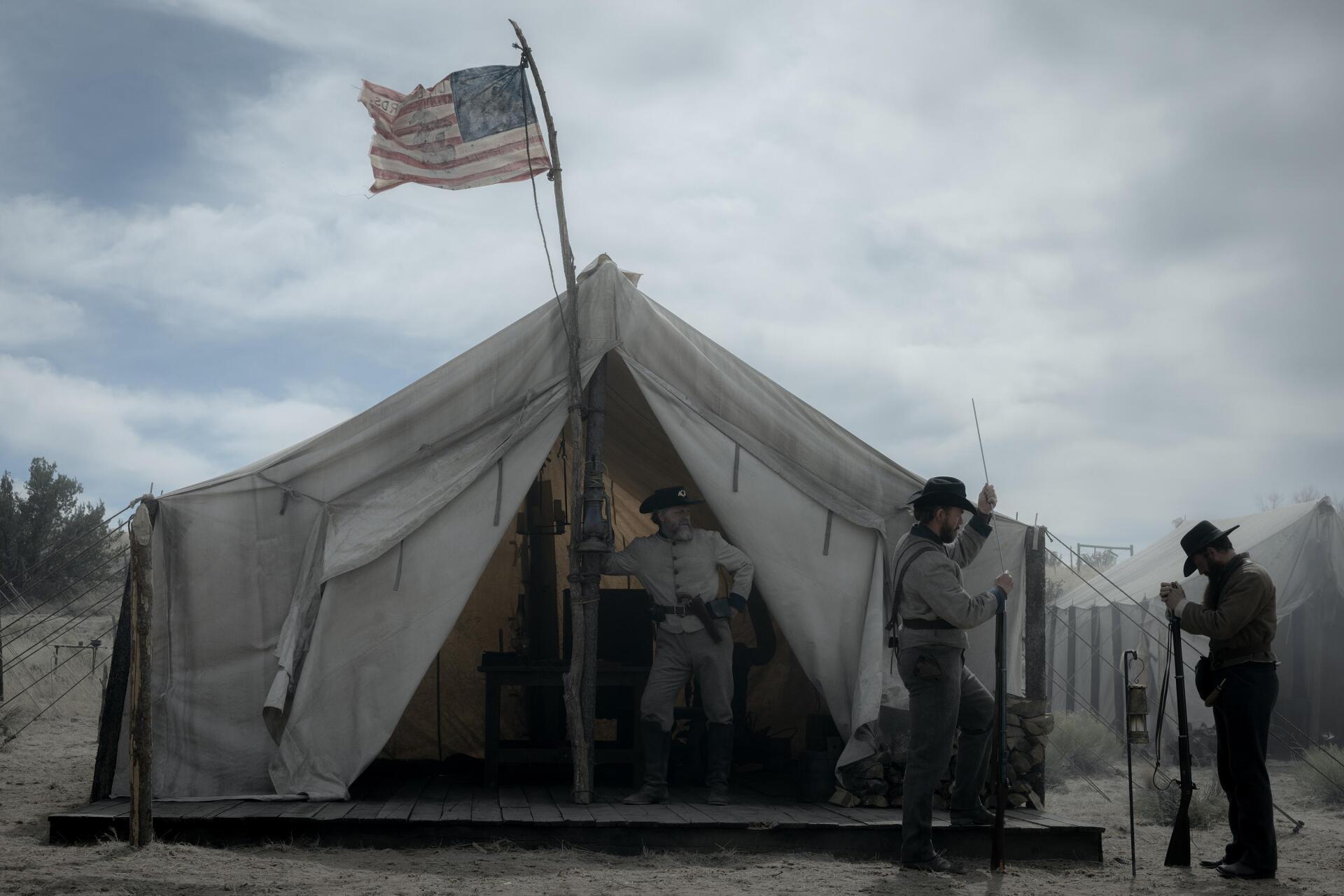 A scene from the TV show American Primeval, featuring a military tent with soldiers in a dusty landscape under a cloudy sky, creating a dramatic and historical atmosphere.