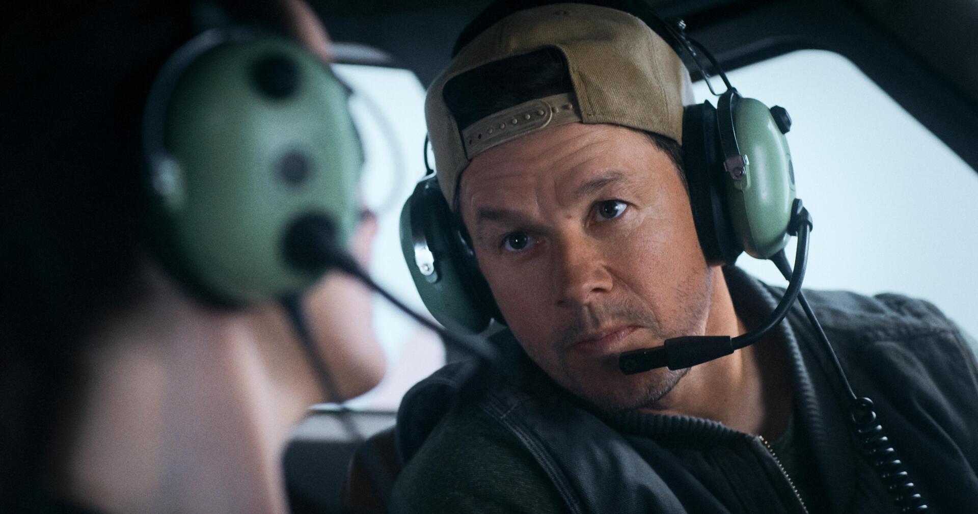 Mark Wahlberg in a scene from the movie Flight Risk, wearing a cap and headset, deeply engaged in conversation. HD desktop wallpaper featuring action-packed drama.