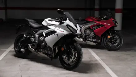 A striking image of two Triumph Daytona 660 motorcycles, one in white and the other in red, set against a minimalist parking garage backdrop. Captured in 4K Ultra HD.