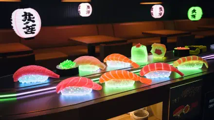 A vibrant display of sushi on a illuminated countertop, showcasing various types including bright salmon and green garnishes, set against a cozy restaurant background. 4K Ultra HD quality wallpaper.