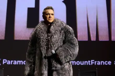 Robbie Williams stands on stage in a luxurious fur coat at the premiere of Better Man (2024), showcasing a striking visual for this 4K Ultra HD desktop wallpaper.