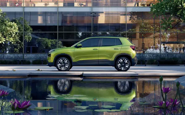 A vibrant green Škoda Kylaq parked beside a serene pond, surrounded by lush greenery, showcased in a stunning 4K Ultra HD desktop wallpaper.