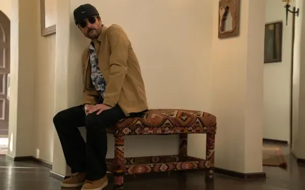 A scene from the 2024 TV show No Good Deed features Luke Wilson sitting on a decorative bench, dressed casually with sunglasses, set in a stylish indoor environment.