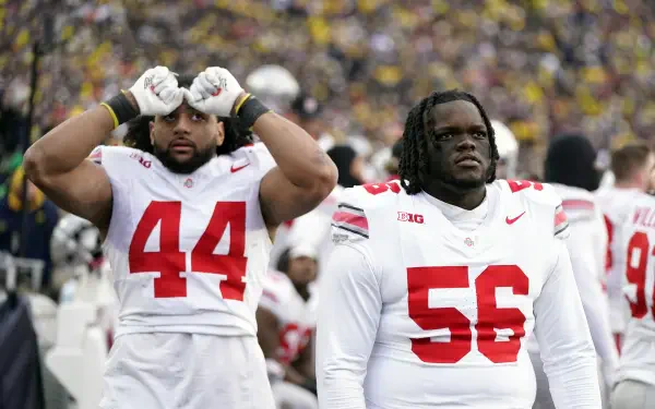 Two Ohio State Buckeyes football players in uniform stand together on the sidelines during a game, showcasing team spirit and intensity in this vibrant 4K Ultra HD wallpaper.