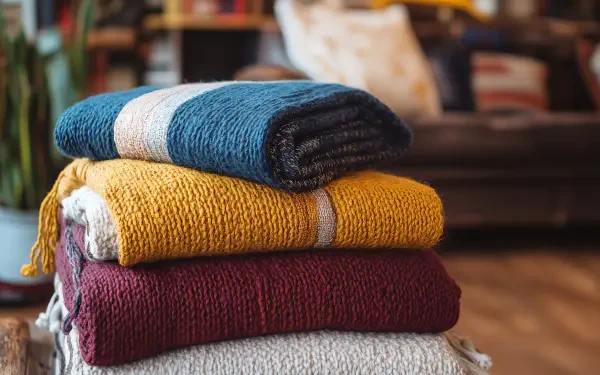 A stack of cozy blankets in rich colors—blue, yellow, maroon, and gray—set against a warm, inviting background, perfect for a 4K Ultra HD desktop wallpaper.