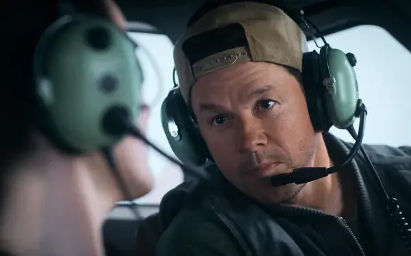 Mark Wahlberg in a scene from the movie Flight Risk, wearing a cap and headset, deeply engaged in conversation. HD desktop wallpaper featuring action-packed drama.