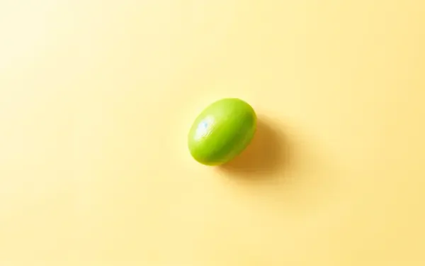 A vibrant green lentil sits against a soft yellow background, creating a striking visual contrast, designed as a 4K Ultra HD PC desktop wallpaper.