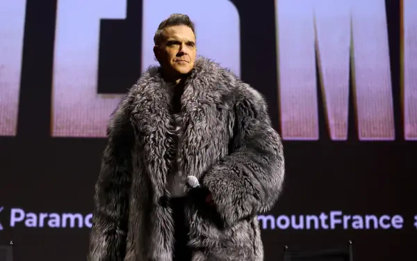Robbie Williams stands on stage in a luxurious fur coat at the premiere of Better Man (2024), showcasing a striking visual for this 4K Ultra HD desktop wallpaper.