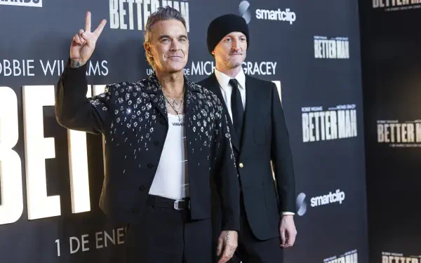 Robbie Williams poses at the premiere of Better Man (2024), showcasing his signature style against a backdrop featuring the movie's branding. 8K Ultra HD wallpaper.