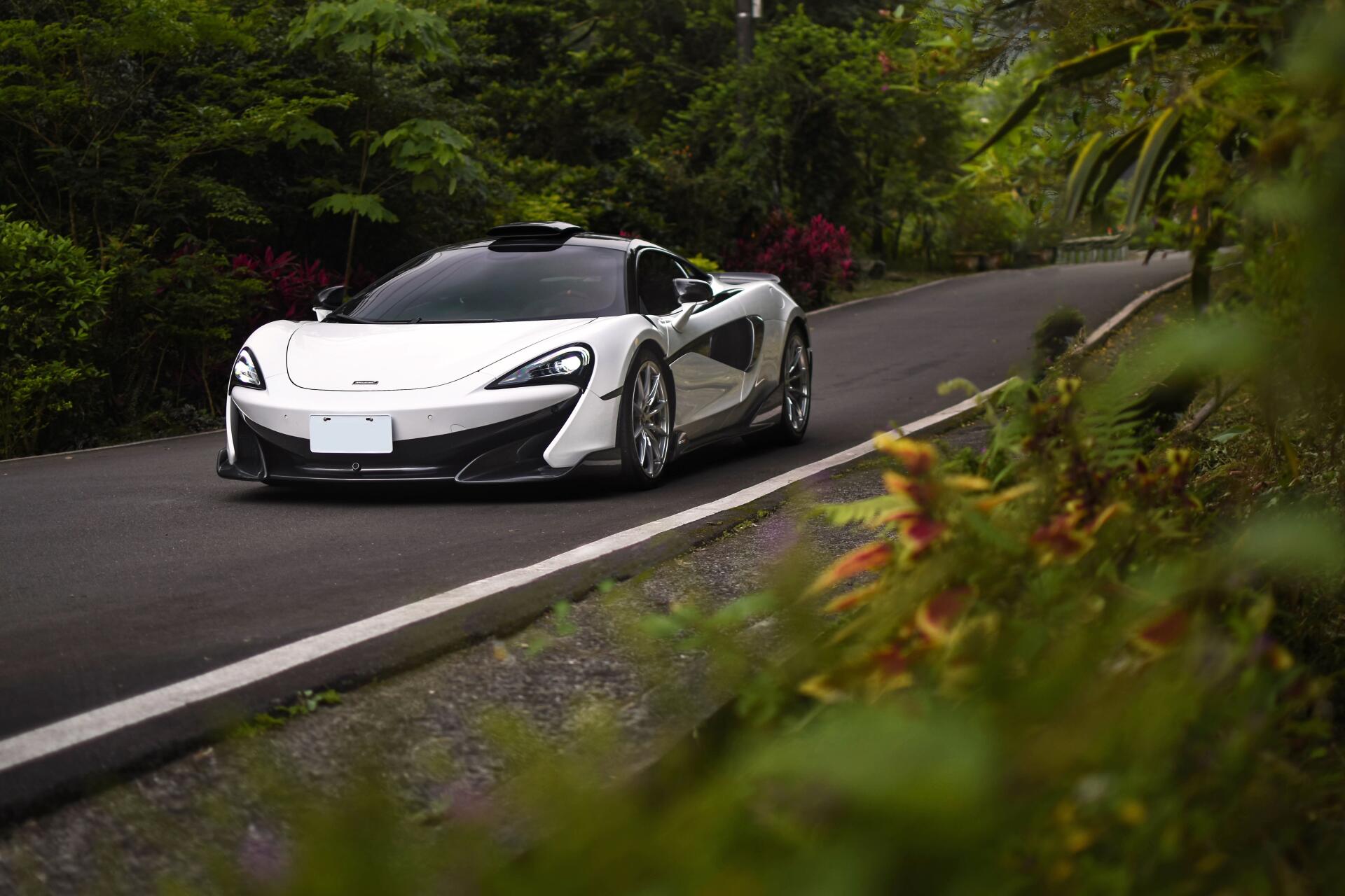 White McLaren P1 supercar on a winding tropical road, lush greenery framing the scene — 5K Ultra HD PC desktop wallpaper background.
