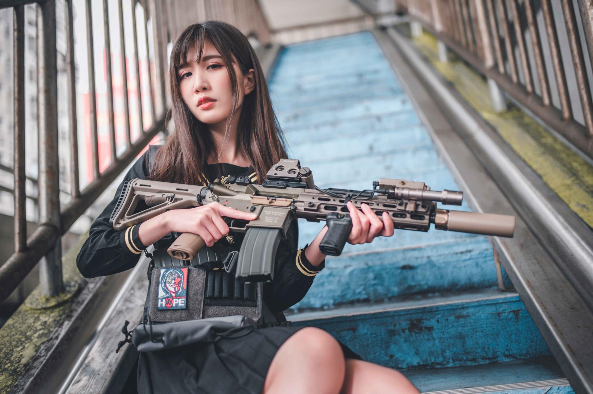 Asian woman seated on worn blue stairs holding a tactical rifle, cinematic 5K Ultra HD PC desktop wallpaper background.