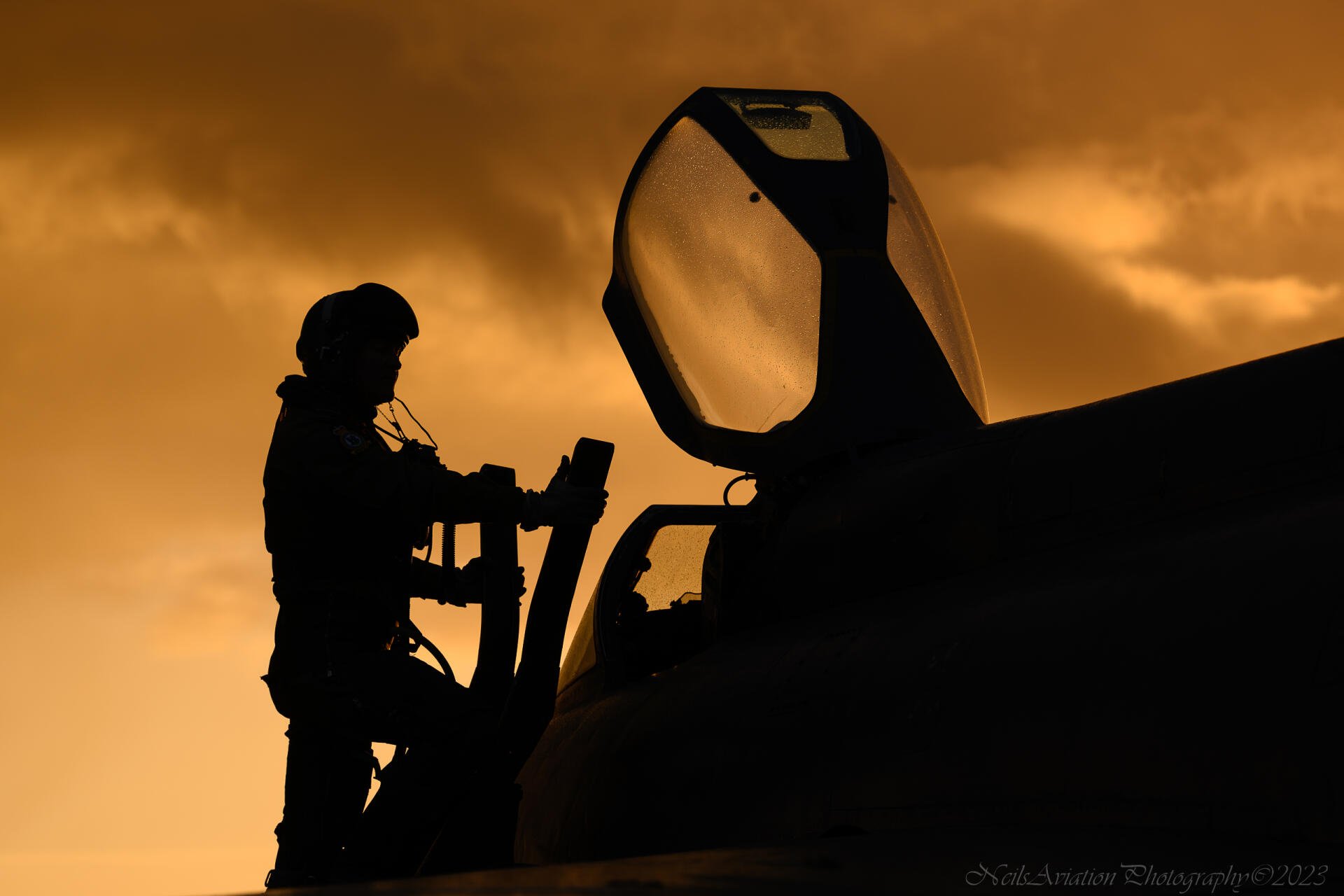Silhouetted military aircraft pilot preparing in cockpit at sunset, captured as an HD desktop wallpaper and background.