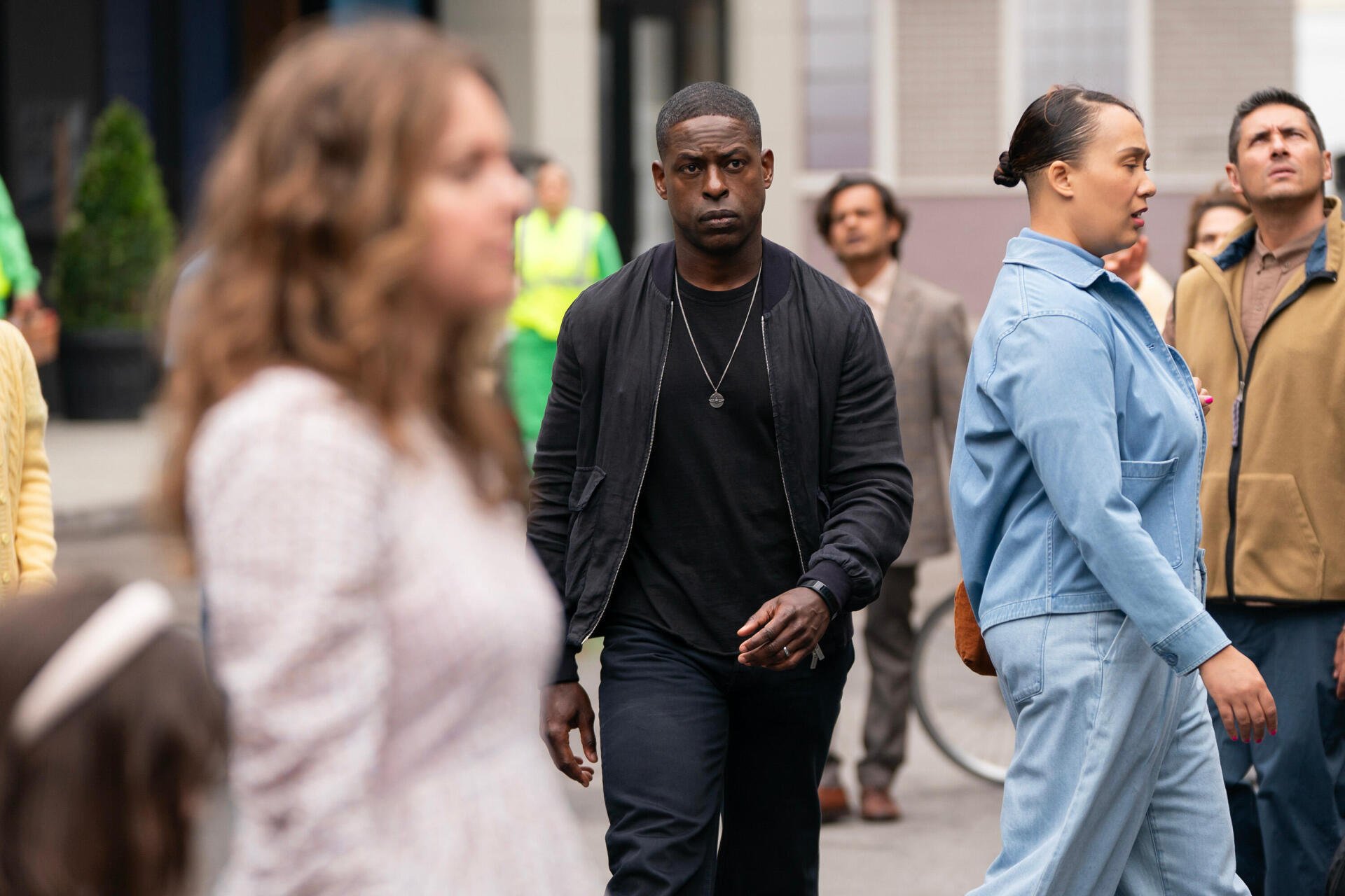 A scene from the TV show Paradise (2025) featuring Sterling K. Brown walking through a bustling crowd, showcasing a vibrant urban backdrop in HD.