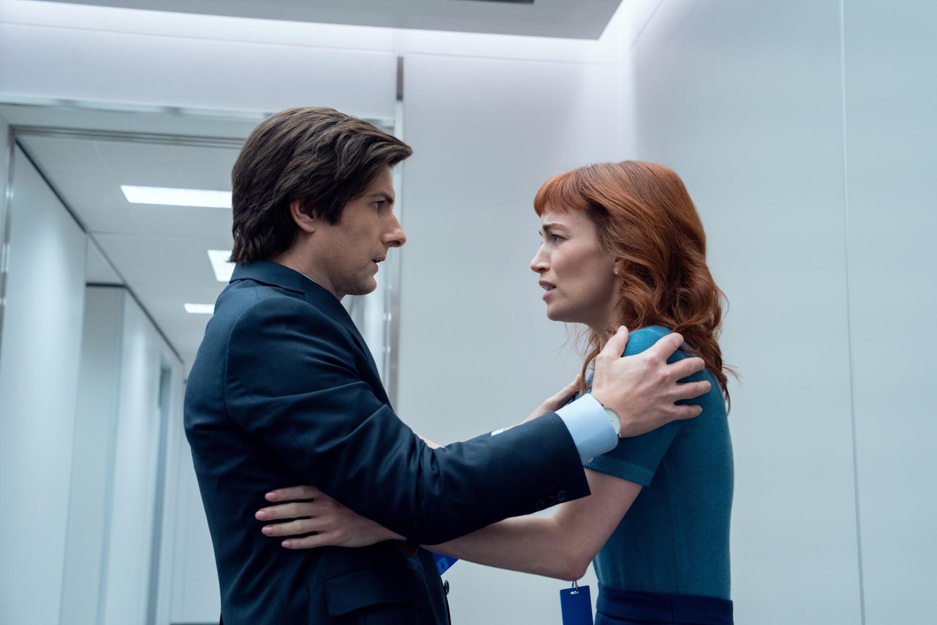 A dramatic moment from the TV show Severance featuring Adam Scott and Britt Lower. The image captures an intense exchange in a sleek, modern office environment.