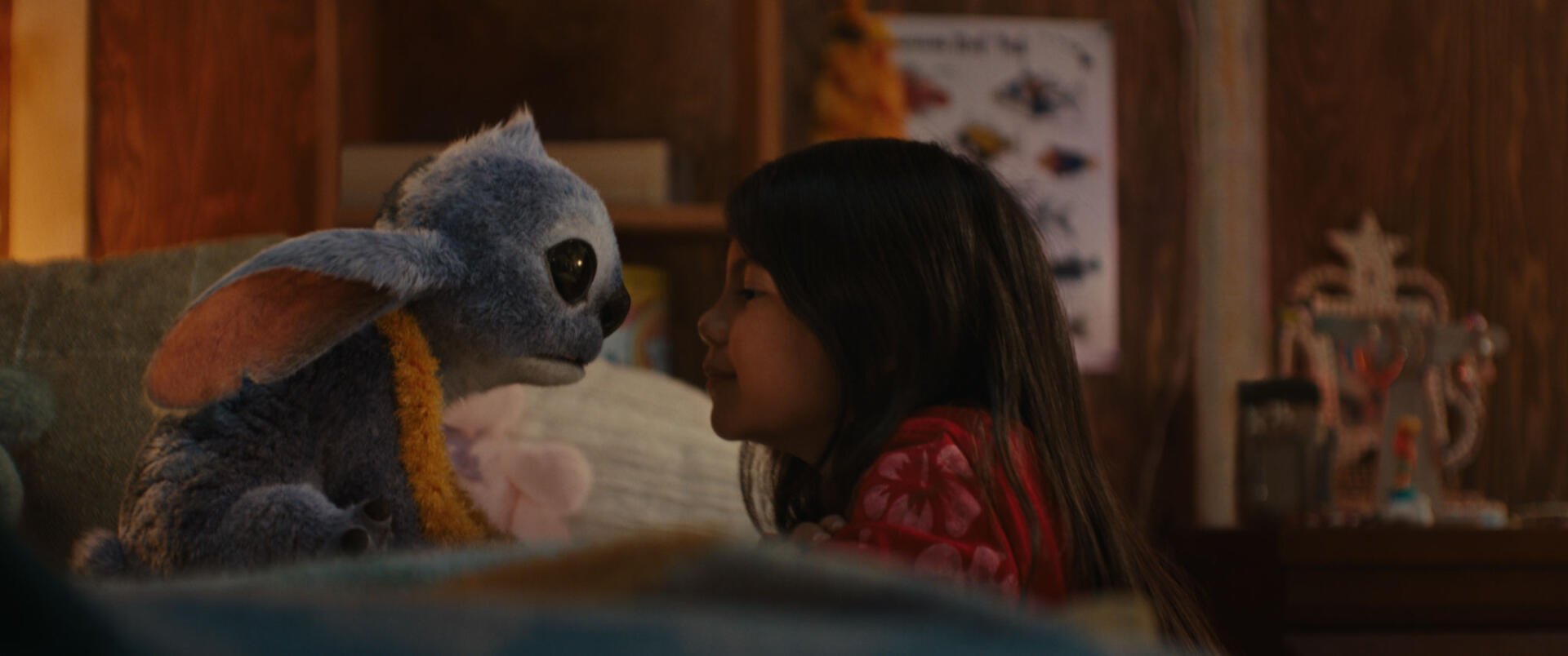 A young girl and her blue alien plush toy share a tender moment in a cozy room, featured in the HD wallpaper for the movie Lilo & Stitch (2025).