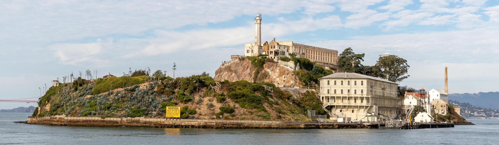 HD desktop wallpaper showcasing Alcatraz Island in California with its historic prison buildings and lighthouse against a partly cloudy sky.