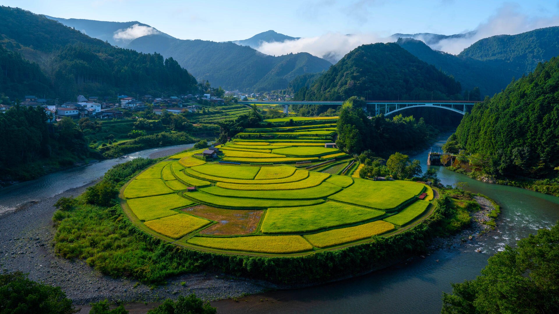Lush terraced grass fields on Aragi Island surrounded by a river and mountains under a clear sky, captured in 4K Ultra HD for a vibrant desktop wallpaper.