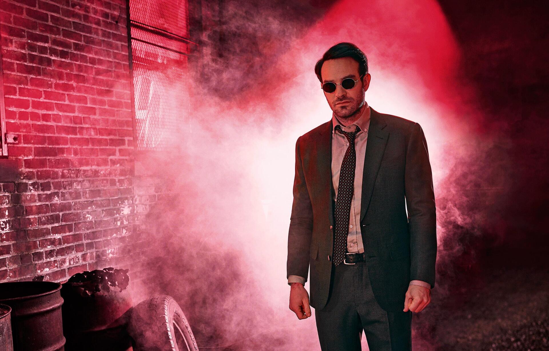 HD PC desktop wallpaper featuring Daredevil in a suit and sunglasses, standing against a red-lit smoky urban backdrop.