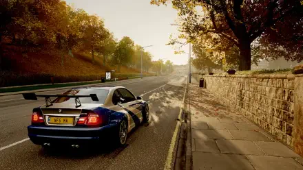 HD PC desktop wallpaper featuring a blue BMW M3 GTR parked on a sunlit, tree-lined road with autumn foliage and a stone wall along the sidewalk.