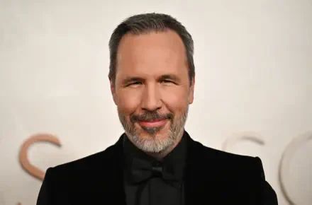 Denis Villeneuve smiles confidently at the Academy Awards, captured in a 4K Ultra HD image, showcasing his stylish appearance against a blurred background.