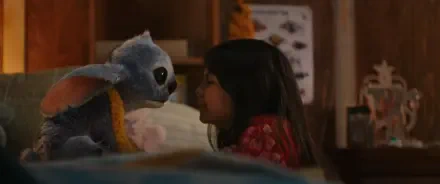 A young girl and her blue alien plush toy share a tender moment in a cozy room, featured in the HD wallpaper for the movie Lilo & Stitch (2025).