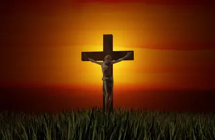 HD desktop wallpaper showing Jesus on the cross at crucifixion, silhouetted against an orange sunset over grass; religious Bible imagery.