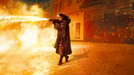 Ballerina (2025) — 8K Ultra HD PC Desktop Wallpaper: lone ballerina in a long coat releasing a fire plume on a snow-dusted, ember-lit street.
