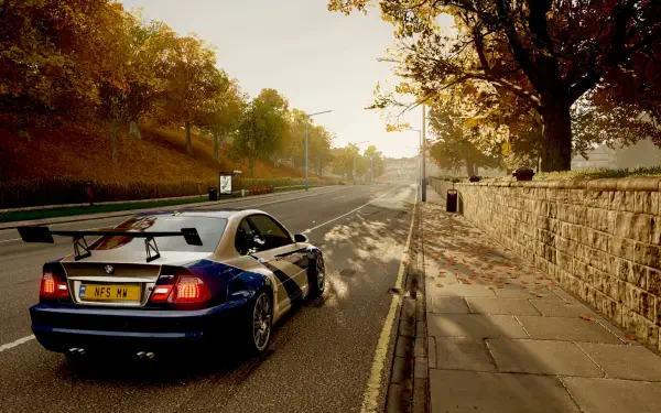 HD PC desktop wallpaper featuring a blue BMW M3 GTR parked on a sunlit, tree-lined road with autumn foliage and a stone wall along the sidewalk.