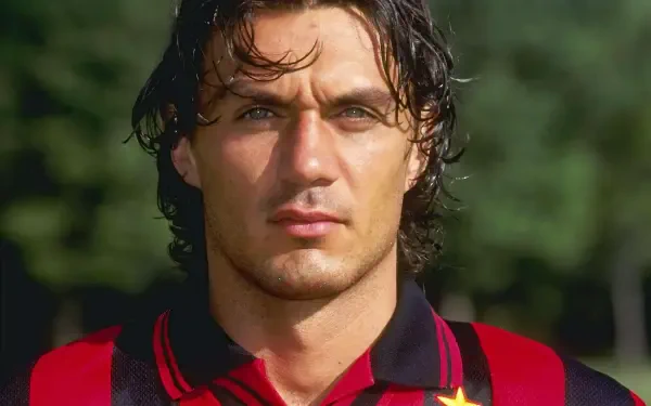 A close-up portrait of Paolo Maldini wearing an A.C. Milan jersey, showcasing his intense gaze and defining features, set against a vibrant outdoor background.