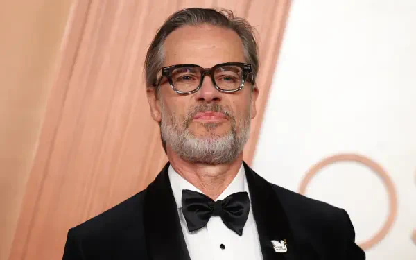 Guy Pearce at the Academy Awards, showcasing a sophisticated look in a tuxedo with glasses, set against an elegant backdrop. This 4K Ultra HD image enhances any desktop background.