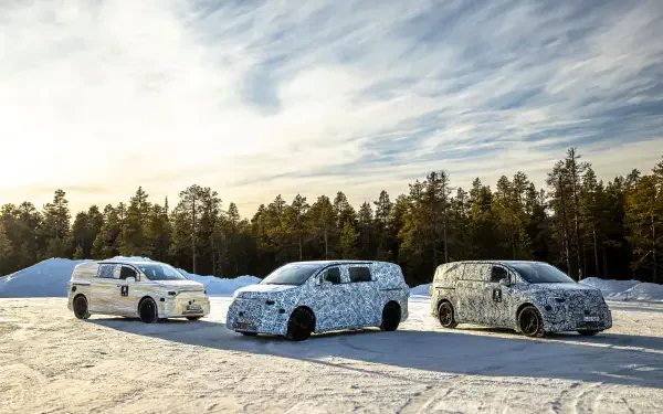 Three camouflaged Mercedes-Benz MPVs lined up on a snowy landscape, showcasing their sleek designs against a backdrop of trees and a clear sky.