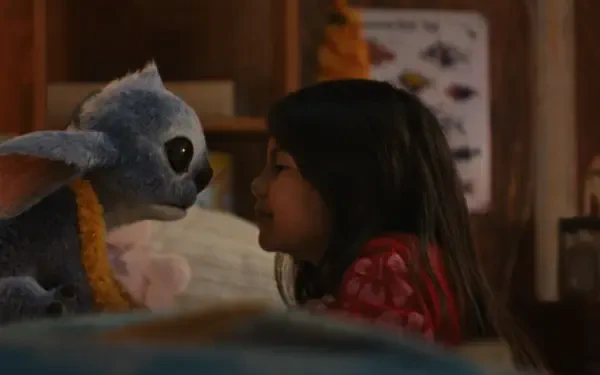 A young girl and her blue alien plush toy share a tender moment in a cozy room, featured in the HD wallpaper for the movie Lilo & Stitch (2025).