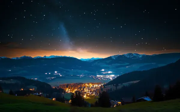 A serene night landscape featuring a town illuminated under a starry sky, with mountains silhouetted in the background, creating a tranquil and breathtaking HD desktop wallpaper.