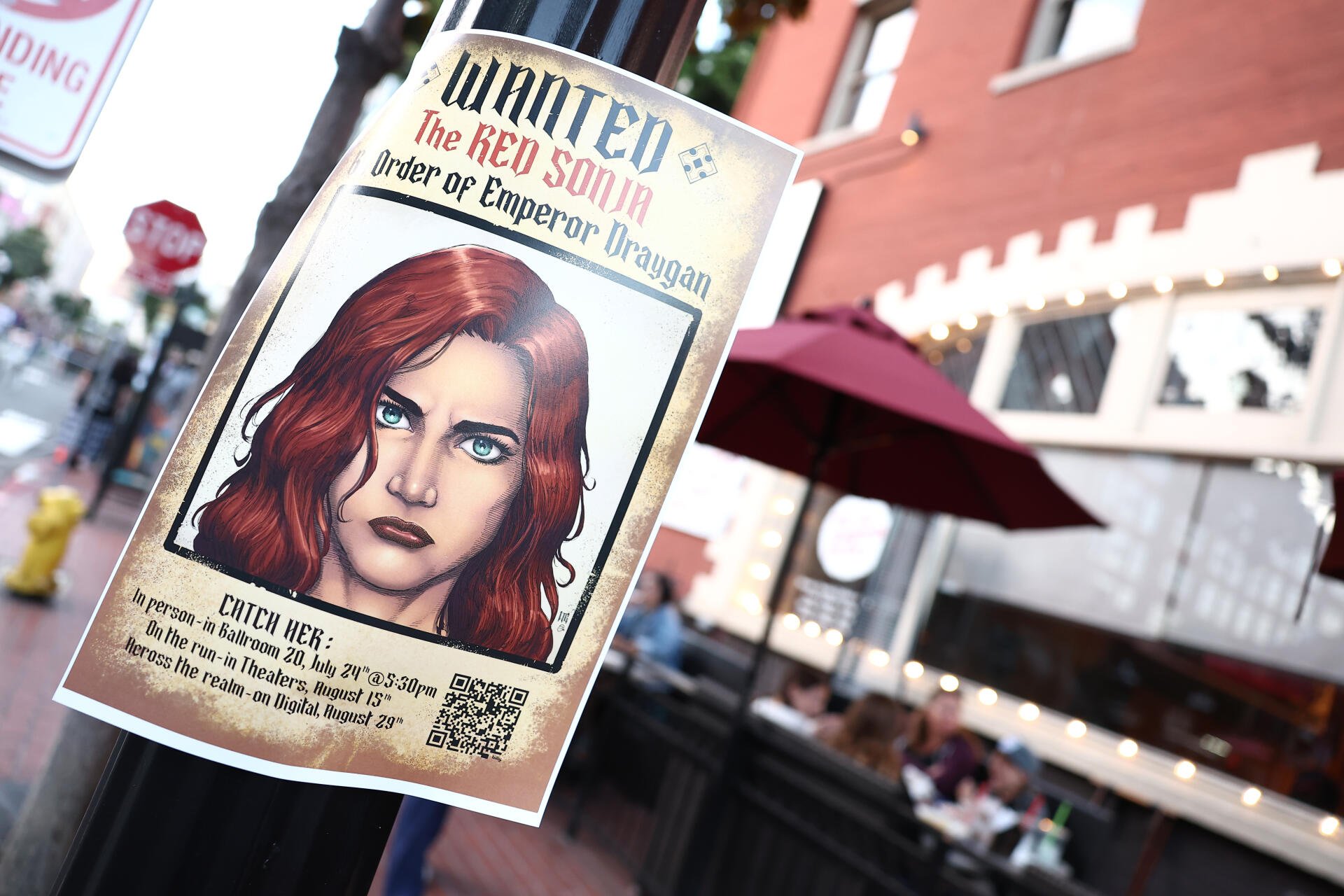 4K Ultra HD movie-style wanted poster of Red Sonja on a street pole — illustrated red-haired warrior with blue eyes, 'WANTED' headline; PC desktop wallpaper background.