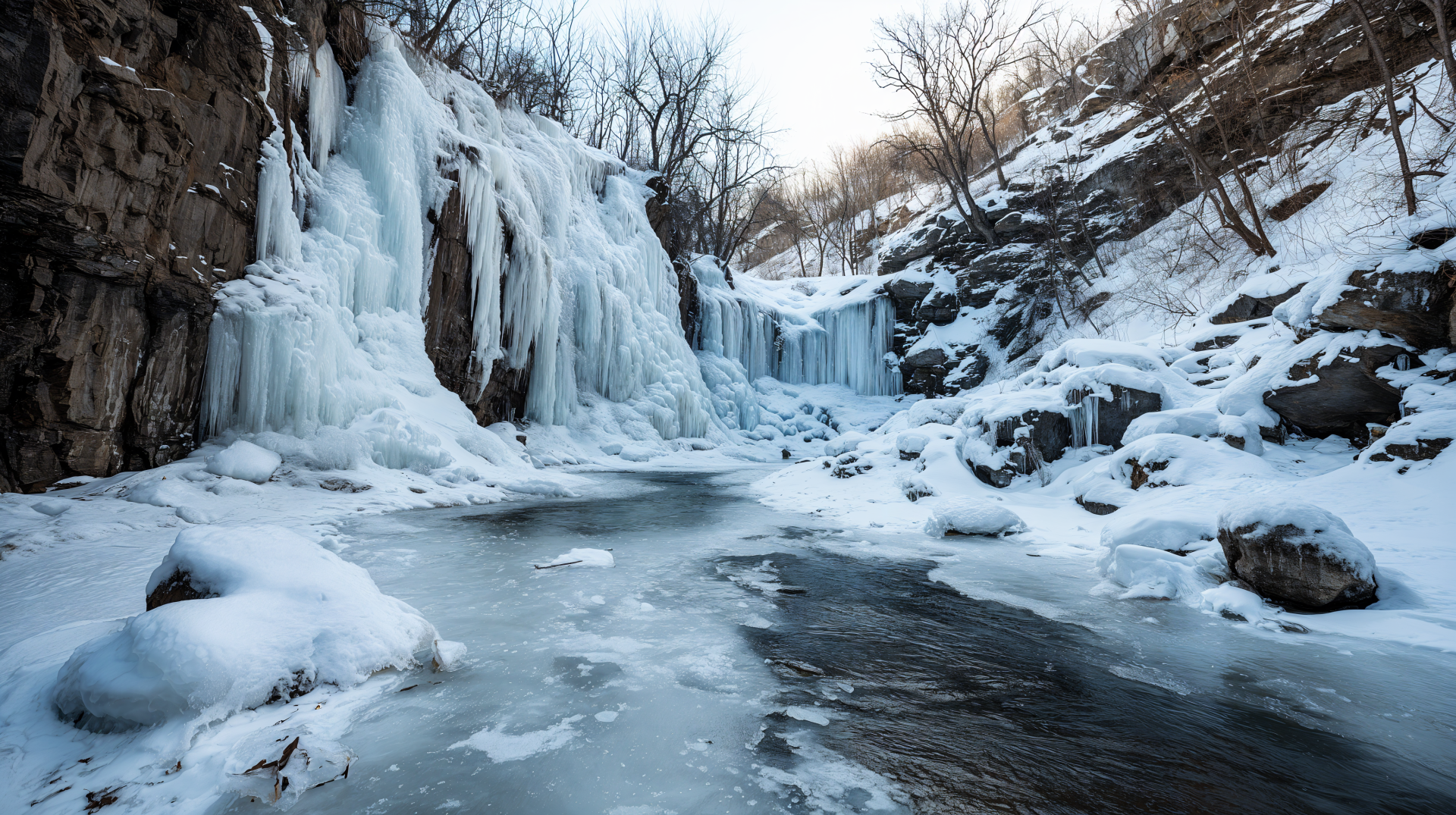 4K Ultra HD PC desktop wallpaper/background showing a nature scene: a frozen waterfall cascading into an icy river amid snow-covered rocks and leafless trees.