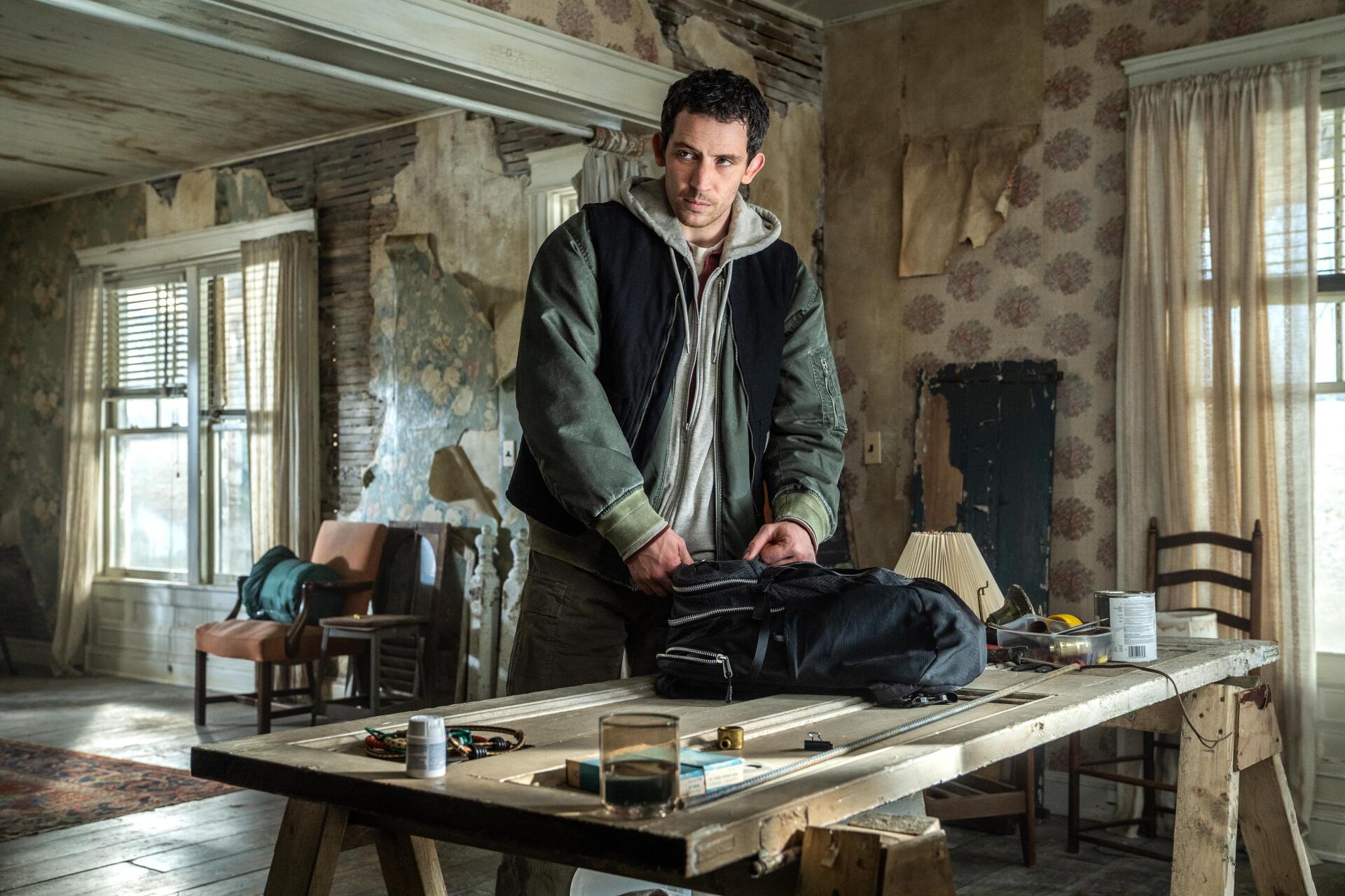 Brooding man in a dilapidated room leans over a cluttered table — cinematic still from the movie Disclosure Day, rendered as a 5K Ultra HD PC desktop wallpaper.