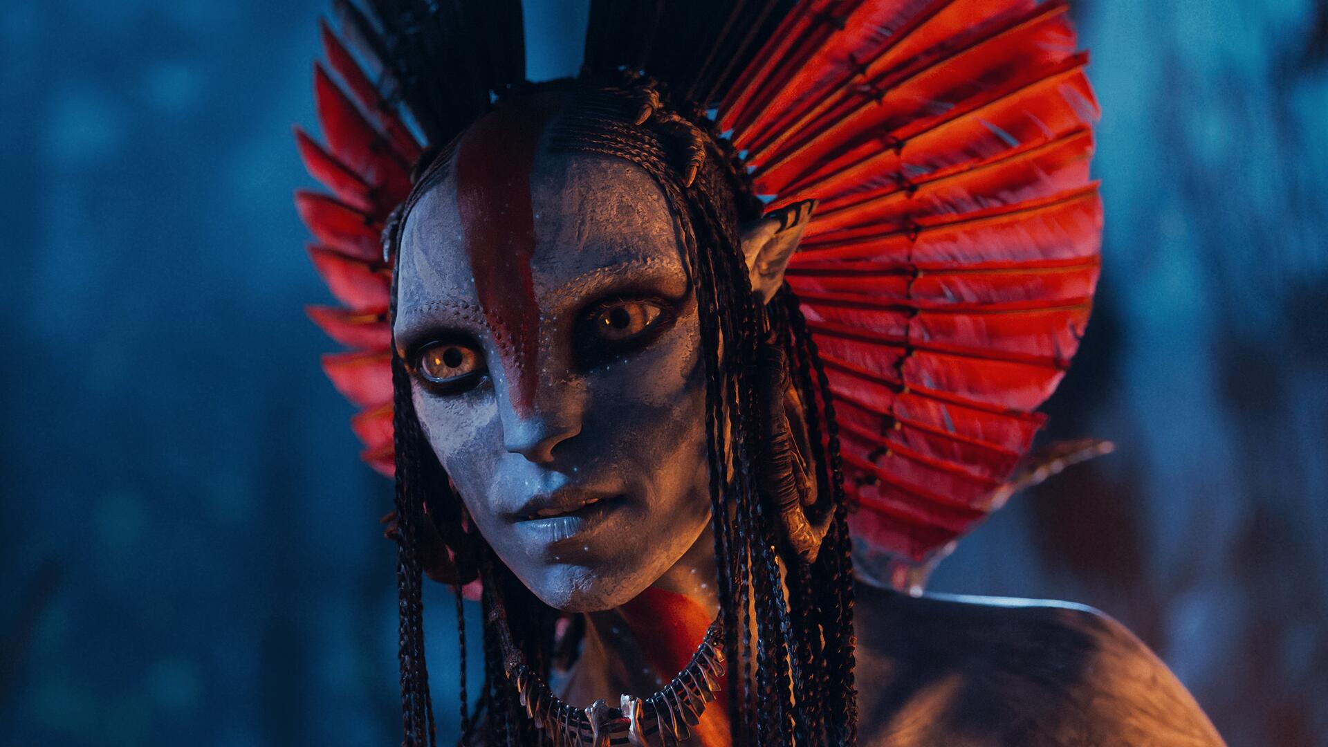 Avatar: Fire and Ash — close-up of a blue-skinned Na'vi with a red feathered headdress and glowing amber eyes, cinematic 4K Ultra HD PC desktop wallpaper/background.