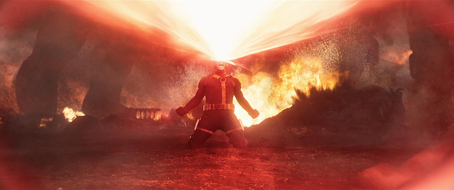 Avengers: Doomsday movie 2K Quad HD PC desktop wallpaper: armored figure kneels as a blinding beam erupts overhead, flames and smoke sweeping across a devastated battlefield.